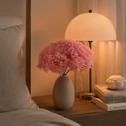 Coral pink preserved hydrangea stems styled in a vase on a bedside table
