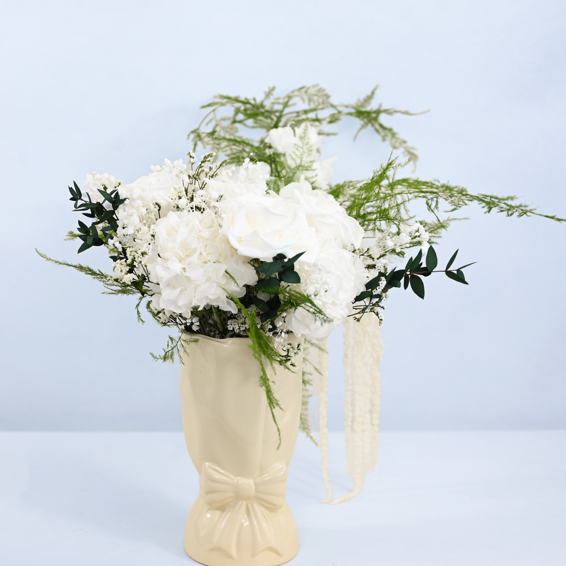 Opal Promise Preserved Flower Bouquet displayed in a cream ceramic bow vase with satin ribbon on a light surface, side view