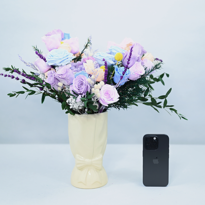 Lavender Sky Preserved Flower Bouquet in a cream ceramic bow vase next to an iPhone for size reference