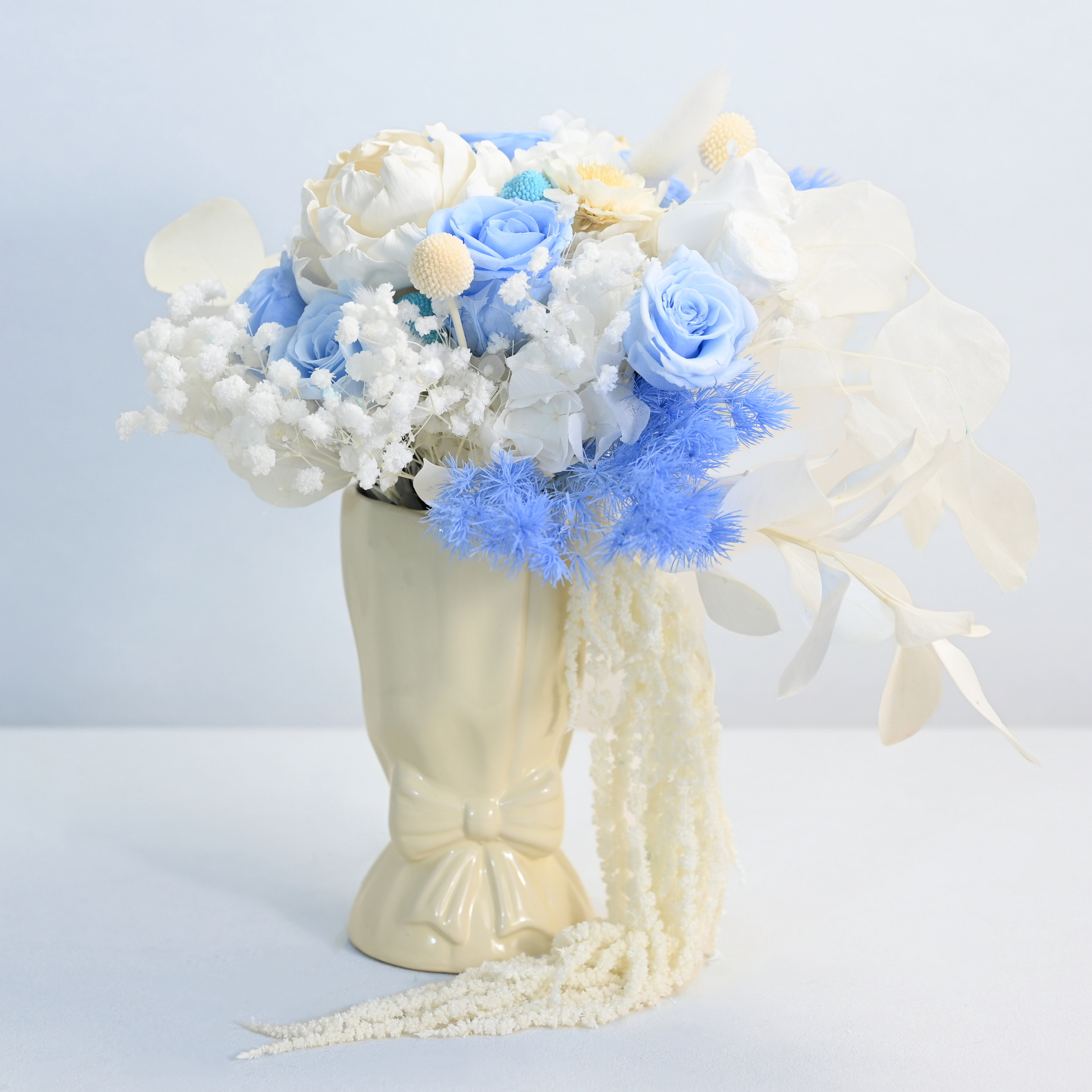 Sapphire Veil Preserved Flower Bouquet displayed in a cream ceramic bow vase with dramatic cascading white amaranthus, front view
