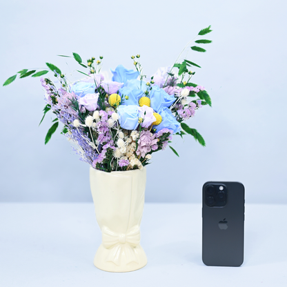 Moonstone Garden Preserved Flower Bouquet in a cream ceramic bow vase next to an iPhone for size reference