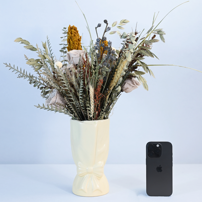 Canyon Muse Preserved Flower Bouquet in ceramic bow vase shown next to an iPhone for size reference