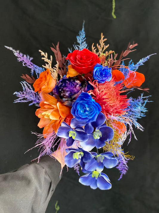 Tourmaline Cascade Preserved Flower Bouquet hand-held arrangement featuring cascading blue orchids, red and blue roses, orange lily, purple peony, and jewel-tone fern fillers