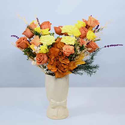 Golden Hour Preserved Flower Bouquet with orange and yellow roses, orange hydrangea and purple lavender displayed in a cream ceramic bow vase, front view