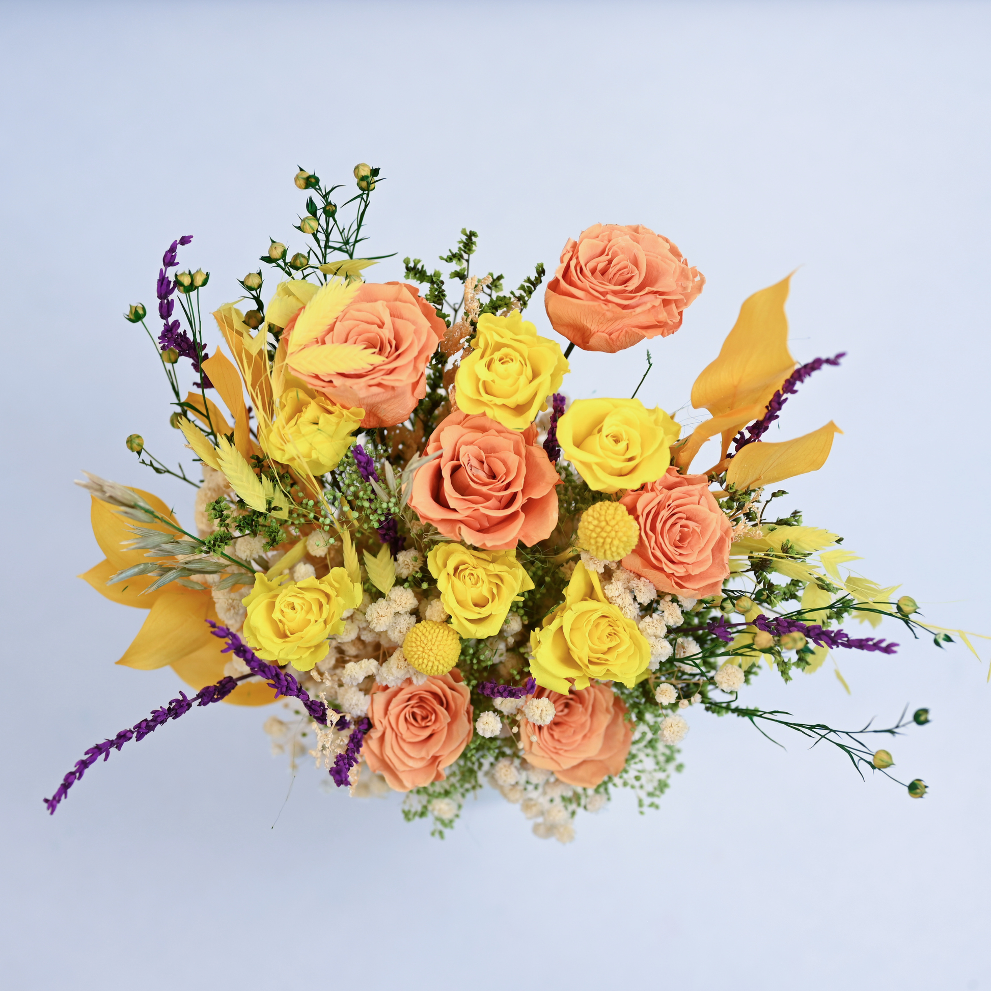 Aerial view of Citrus Meadow Preserved Flower Bouquet showing orange and yellow roses, craspedia, ruscus leaves and purple lavender