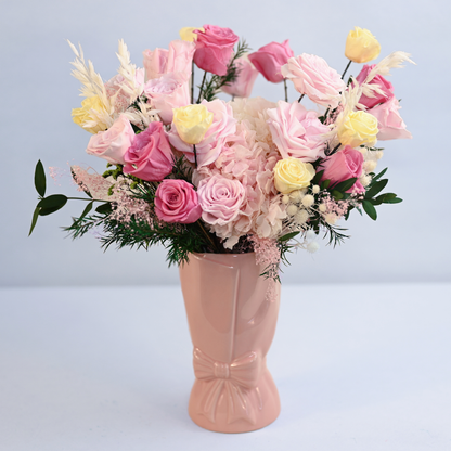 Coral Blush Preserved Flower Bouquet with pink and cream yellow roses, blush hydrangea and pampas grass in a pink ceramic bow vase, front view