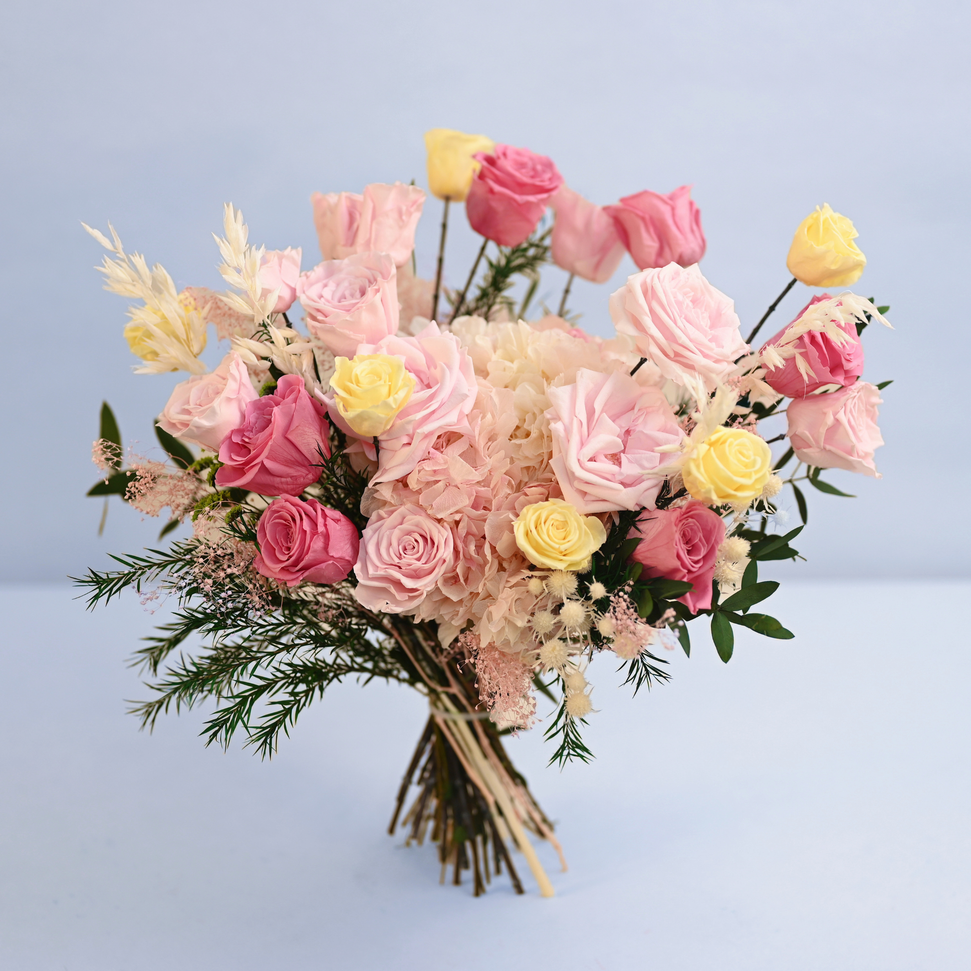 Coral Blush Preserved Flower Bouquet standing upright showing full arrangement of pink and yellow roses with hydrangea, oat grass and hypericum berry, front view
