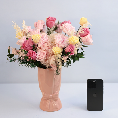Coral Blush Preserved Flower Bouquet in pink ceramic bow vase shown next to an iPhone for size reference