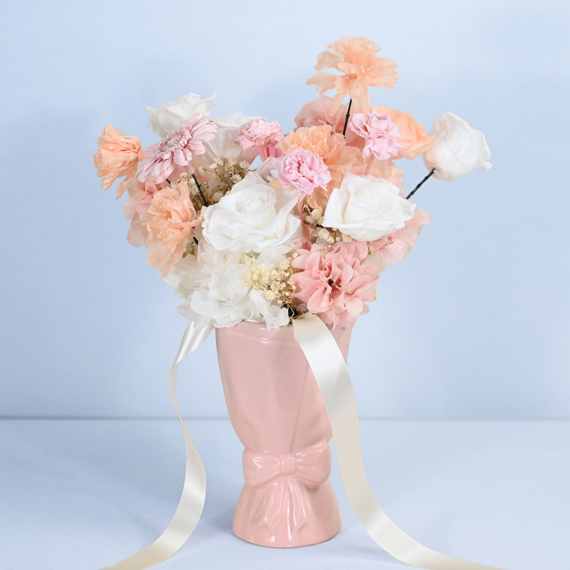 Blush Reverie Preserved Flower Bouquet displayed in a pink ceramic bow vase with cream satin ribbon, front view
