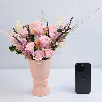 Wild Rose Preserved Flower Bouquet in a pink ceramic bow vase next to an iPhone for size reference