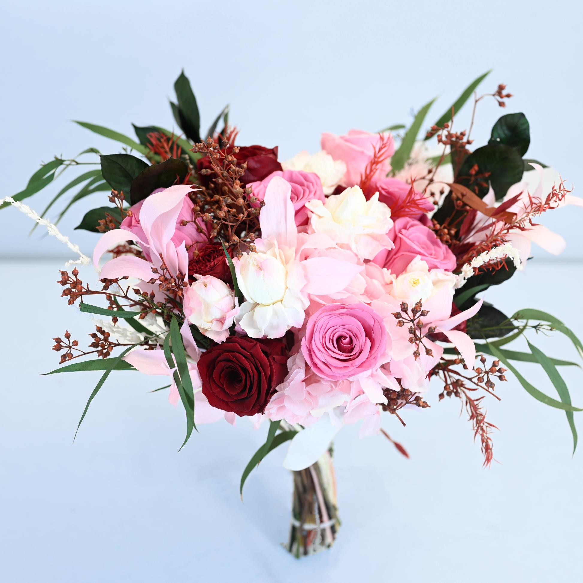 Crimson Blush Preserved Flower Bouquet featuring deep red and pink roses, blush hydrangea, white lisianthus and pepper berry branches, front view