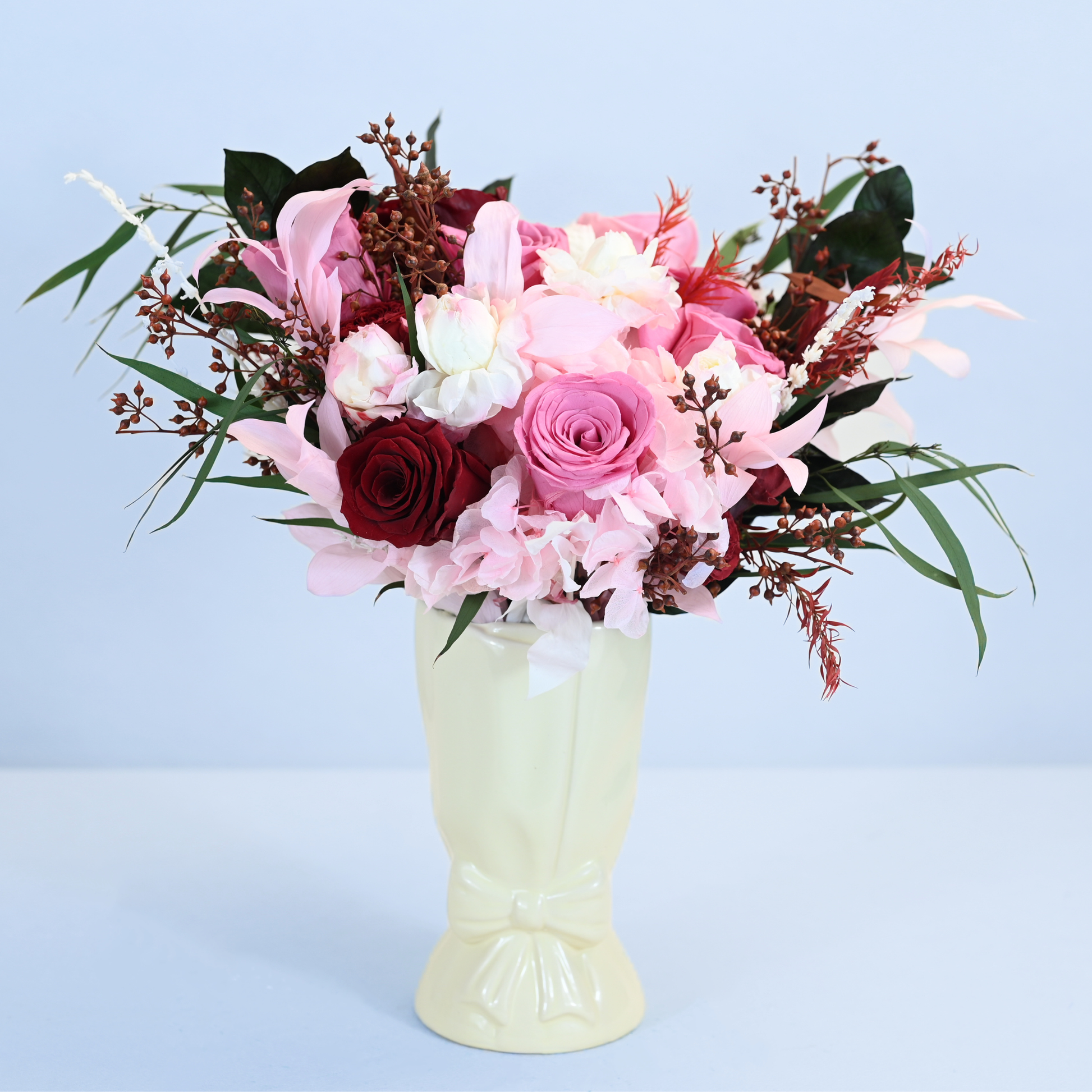 Crimson Blush Preserved Flower Bouquet displayed in a cream ceramic bow vase, front view