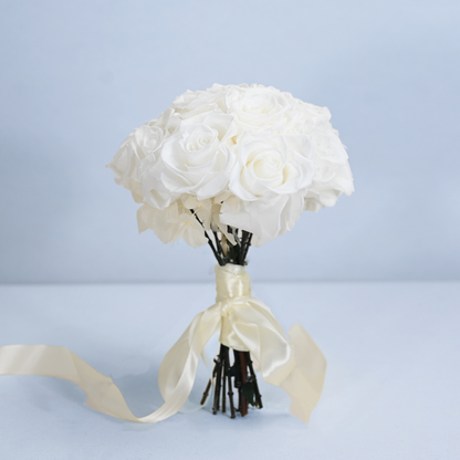Opal Preserved Rose Bouquet standing upright on a light surface with cream satin ribbon, front view against soft blue background