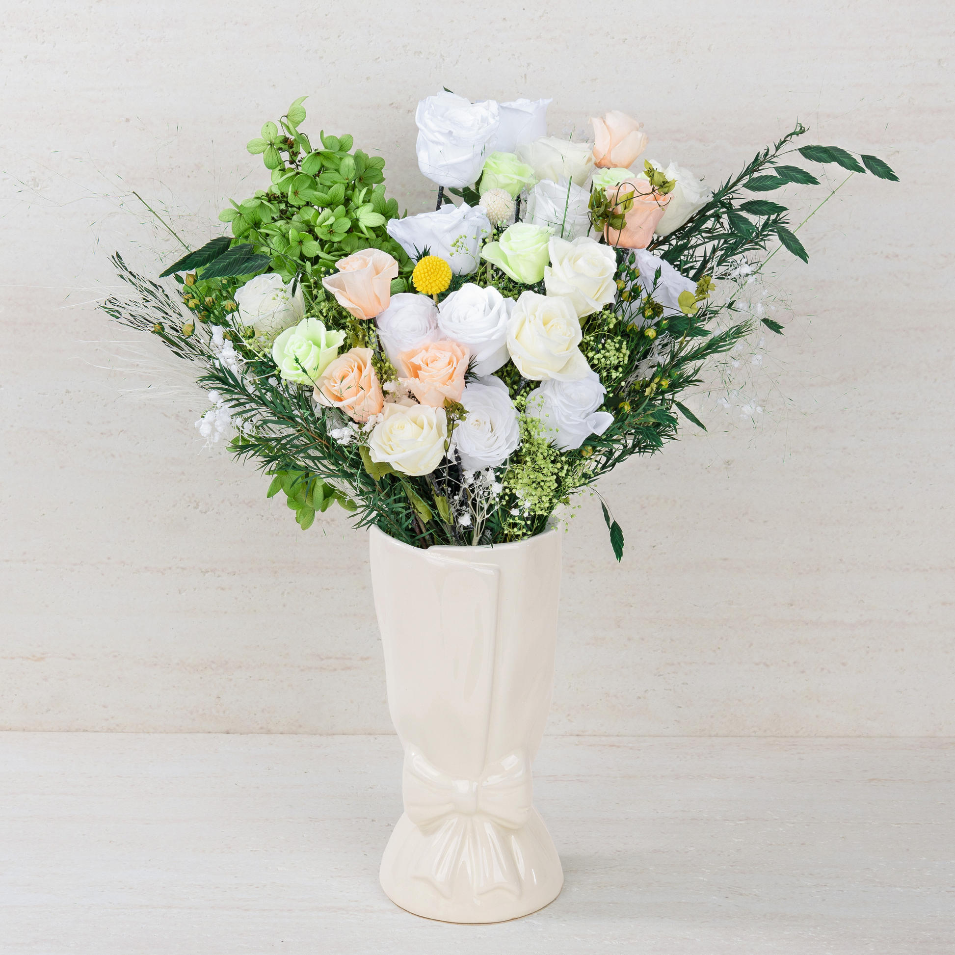 Opal Bloom Preserved Flower Bouquet with white, cream and peach roses, green hydrangea and lush mixed foliage displayed in a white ceramic bow vase, front view