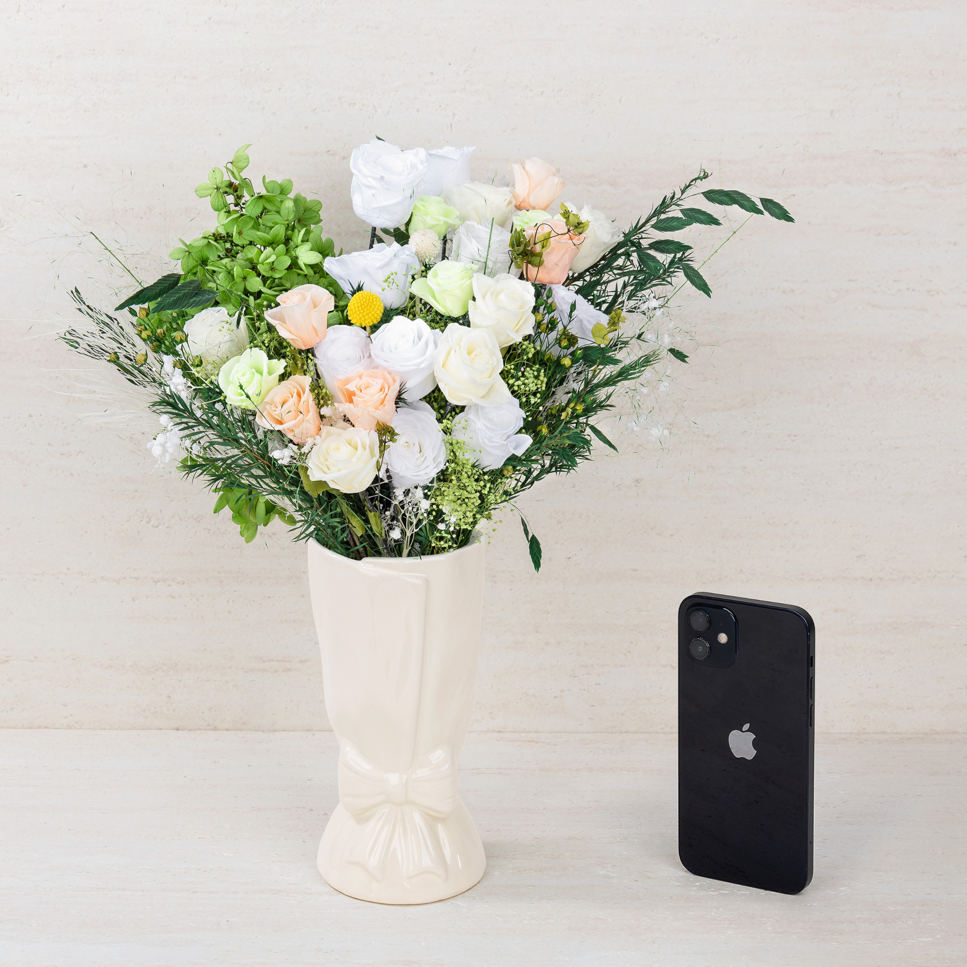 Opal Bloom Preserved Flower Bouquet in white ceramic bow vase shown next to an iPhone for size reference, against a neutral linen background