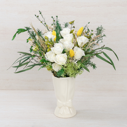 Opal Meadow Preserved Flower Bouquet with white roses, yellow craspedia and lush green foliage displayed in a white ceramic bow vase, front view